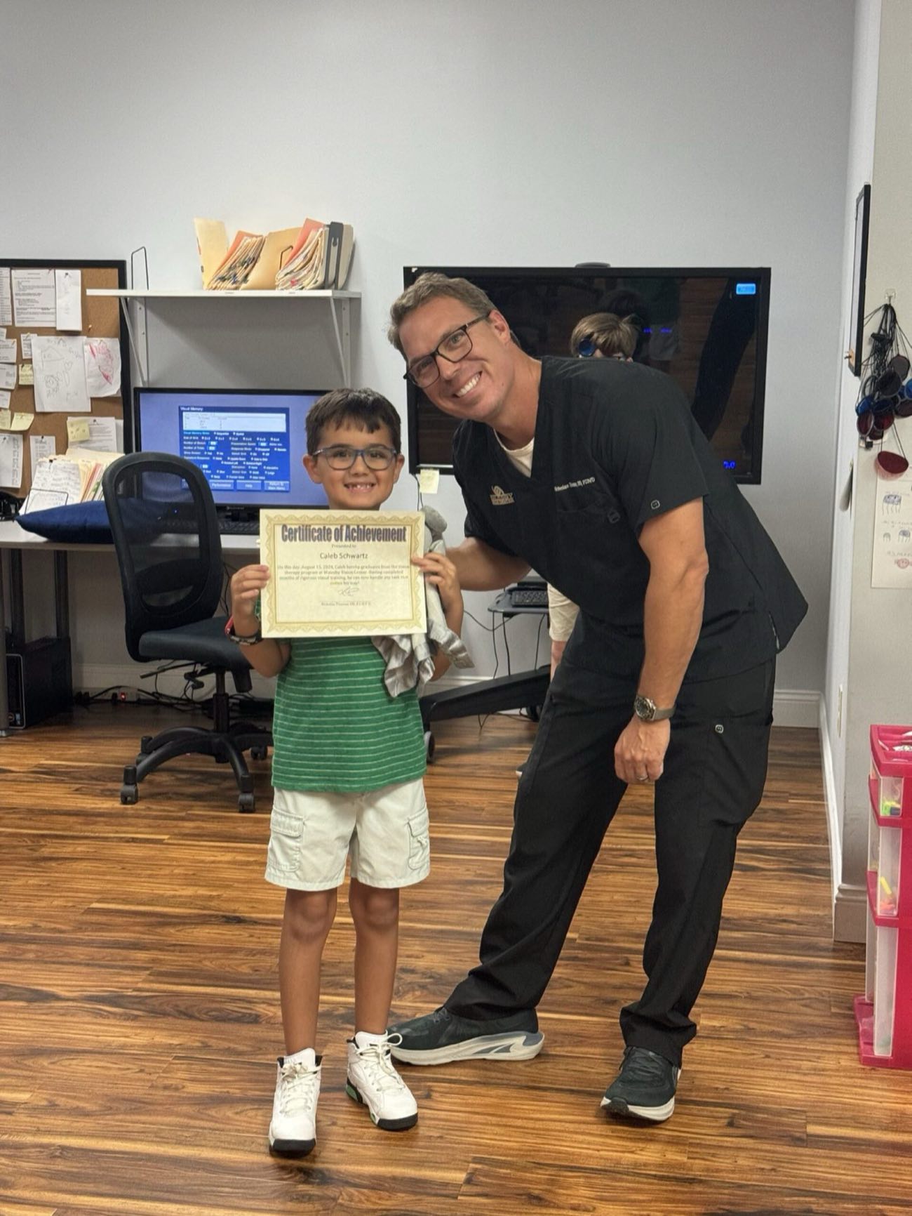 Caleb holding his graduation certificate beside Dr. Thomas
