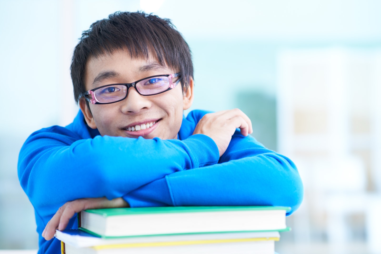 A teenager smiling over a stack of books